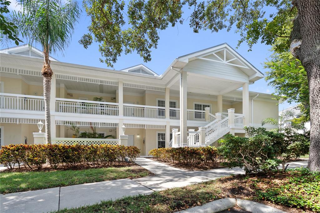 A two-story apartment building features a white staircase, covered balconies, and landscaped shrubbery — 3702 54TH DRIVE W UNIT 102, BRADENTON, FL