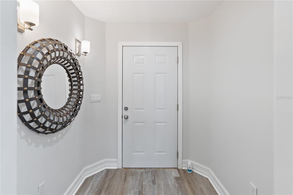 An entryway features a white door, light wood-look flooring, and a large circular wall mirror — 3702 54TH DRIVE W UNIT 102, BRADENTON, FL