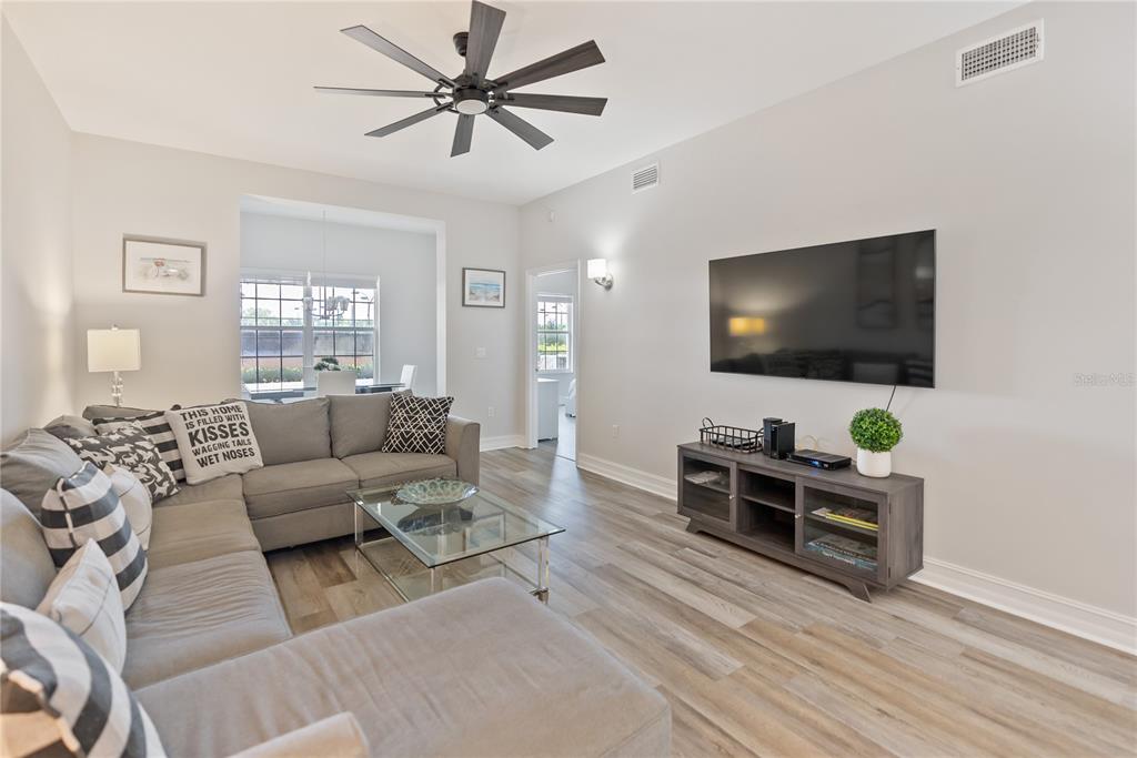 A living room features a grey sectional sofa, a glass coffee table, and a wall-mounted television — 3702 54TH DRIVE W UNIT 102, BRADENTON, FL