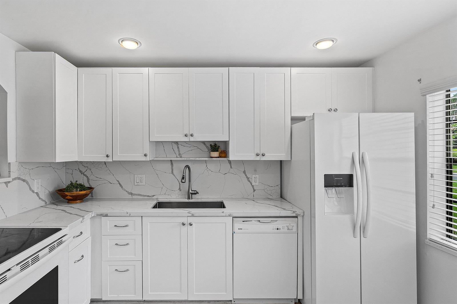 A kitchen features white cabinets, marble-patterned countertops and backsplash, a stainless steel sink, and appliances — 21506 Juego Circle # 28e, Boca Raton FL 33433, BOCA RATON, FL