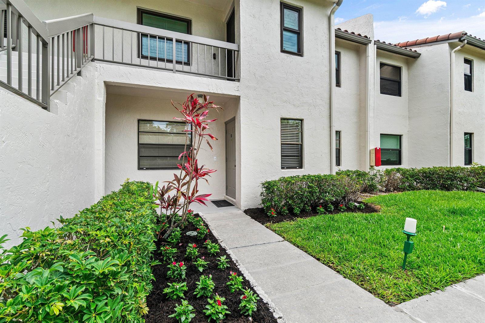 A two-story apartment building exterior features a concrete walkway, landscaping, and a second-floor balcony — 21506 Juego Circle # 28e, Boca Raton FL 33433, BOCA RATON, FL