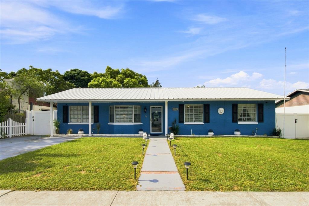 A blue, single-story brick house features a white metal roof and a central walkway — 1206 TULIPWOOD DRIVE, SEFFNER, FL