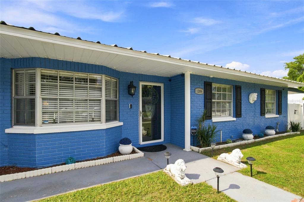 A blue brick house features a bay window, a front door, and decorative lion statues — 1206 TULIPWOOD DRIVE, SEFFNER, FL