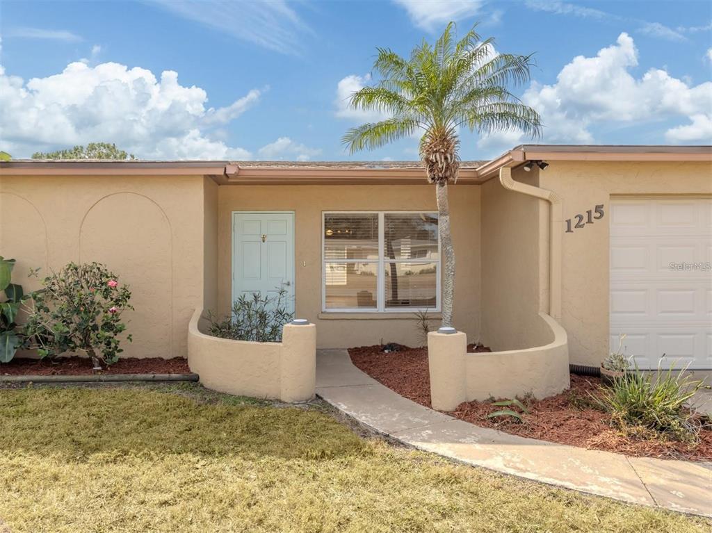 The exterior of a tan house features a light blue front door and a palm tree — 1215 MANGO AVENUE, VENICE, FL