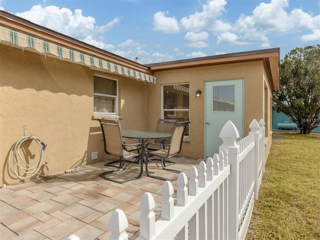 A paved patio with a dining set sits beside a house with a white fence — 1215 MANGO AVENUE, VENICE, FL