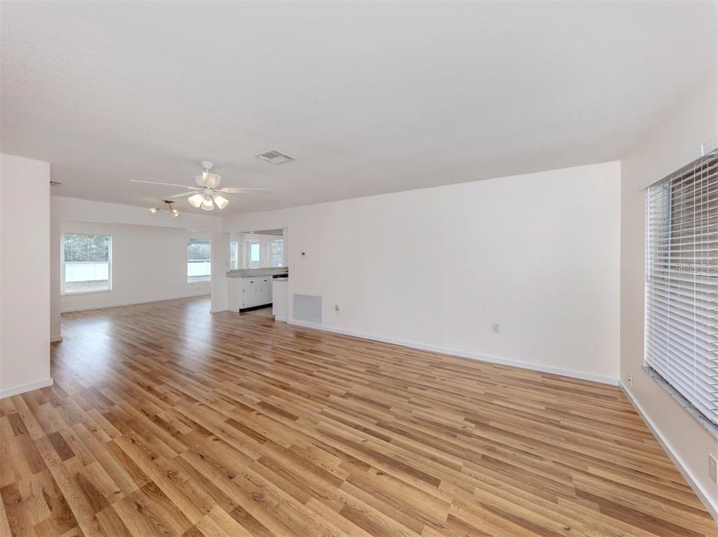A spacious living room features light wood-look flooring, white walls, and a ceiling fan — 1215 MANGO AVENUE, VENICE, FL