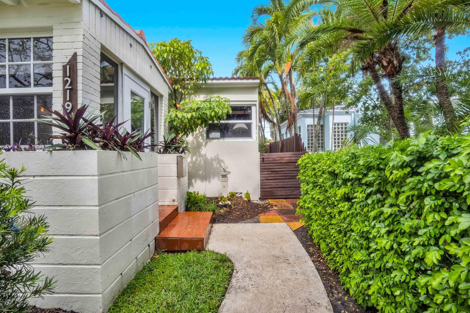 A white house exterior features a concrete walkway, a tiled entrance, and a green hedge — 1219 N Lakeside Drive, FL 33460, FL