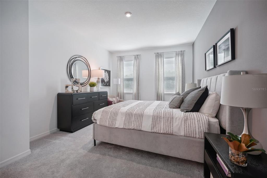 A bedroom features a gray upholstered bed, a black dresser, and two windows with curtains — 6763 WINTERBERRY DRIVE, LAKE HAMILTON, FL