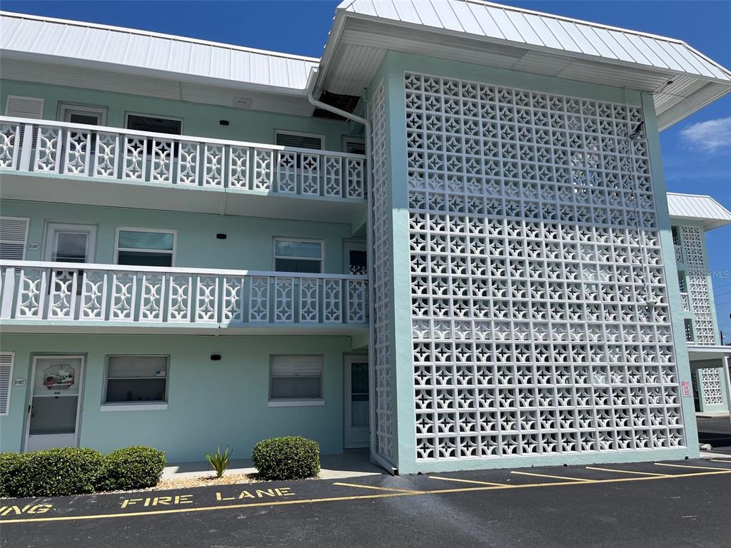A three-story apartment building features light blue exterior walls and decorative white breeze block screens — 325 N CAUSEWAY UNIT D108, NEW SMYRNA BEACH, FL