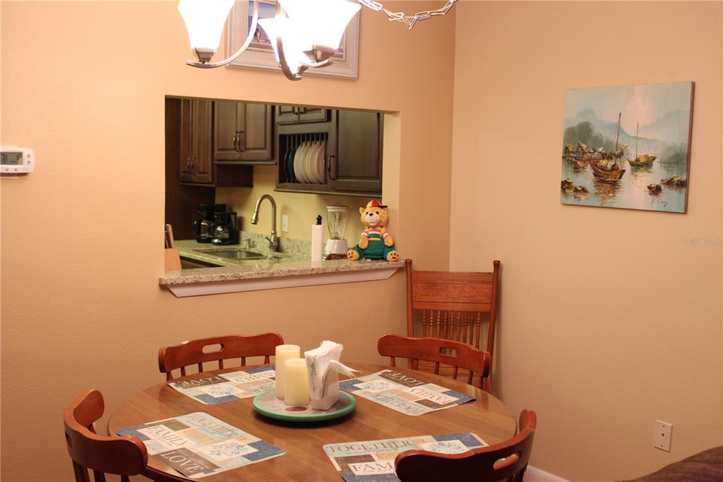 A dining area with a round wooden table, chairs, and a pass-through to the kitchen — 325 N CAUSEWAY UNIT D108, NEW SMYRNA BEACH, FL