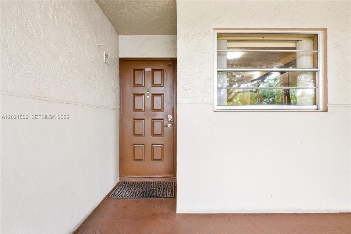 A brown front door with eight panels sits on a covered porch beside a window — 9501 Seagrape Dr # 102, Davie FL 33324, DAVIE, FL