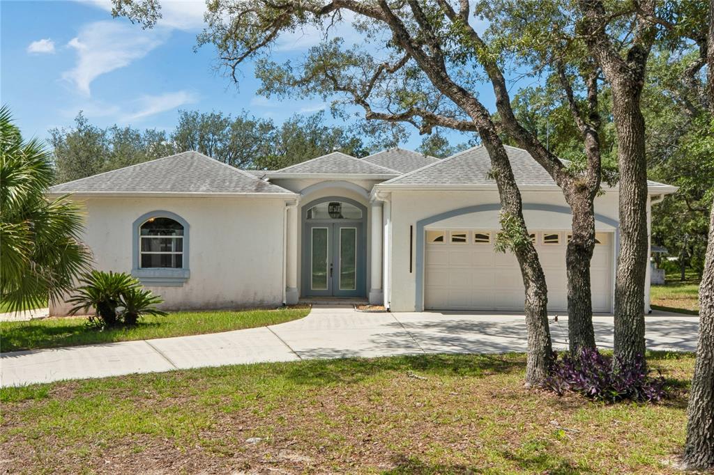 A single-story house with a white stucco exterior, a two-car garage, and a double-door entrance — 12408 KANAWHA DRIVE, WEEKI WACHEE, FL