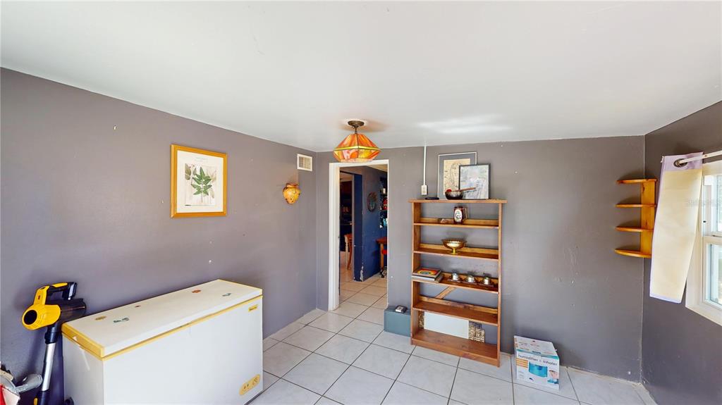 A room with gray walls, white tile flooring, a chest freezer, and a wooden bookshelf — 5651 6TH STREET, ZEPHYRHILLS, FL