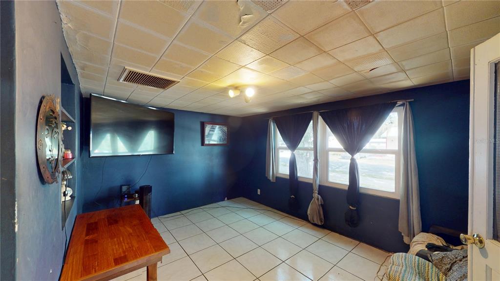 A room with blue walls, white tile flooring, a drop ceiling, and a wall-mounted television — 5651 6TH STREET, ZEPHYRHILLS, FL