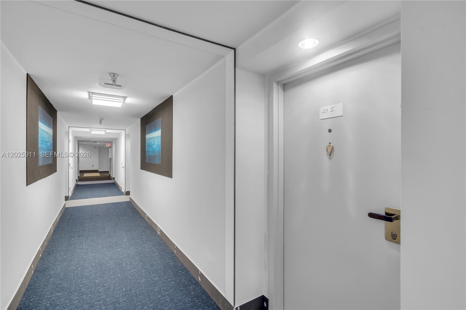 A hallway with blue carpet, white walls, and a door labeled 23 I — 555 NE 15th St # 23I, Miami FL 33132, MIAMI, FL