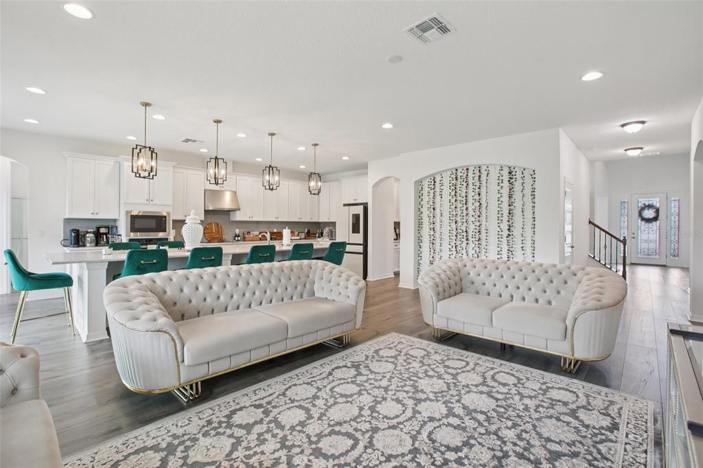 An open-concept living room and kitchen featuring tufted sofas, a patterned rug, and white cabinetry — 9508 PYRENEES PLACE, SEFFNER, FL