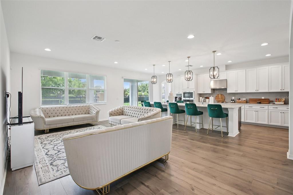 An open-concept living room and kitchen feature white cabinetry, green bar stools, and tufted sofas — 9508 PYRENEES PLACE, SEFFNER, FL