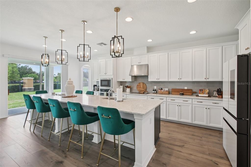 A kitchen features white cabinets, a large island with teal barstools, and wood-look flooring — 9508 PYRENEES PLACE, SEFFNER, FL