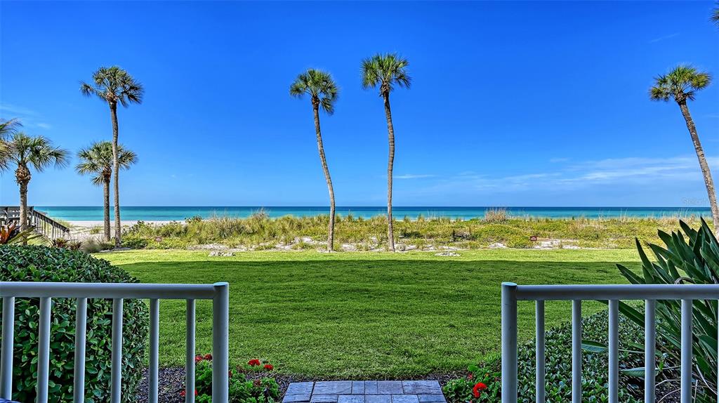 A view from a patio overlooking a grassy lawn, palm trees, and the ocean — 4325 GULF OF MEXICO DRIVE UNIT 103, LONGBOAT KEY, FL