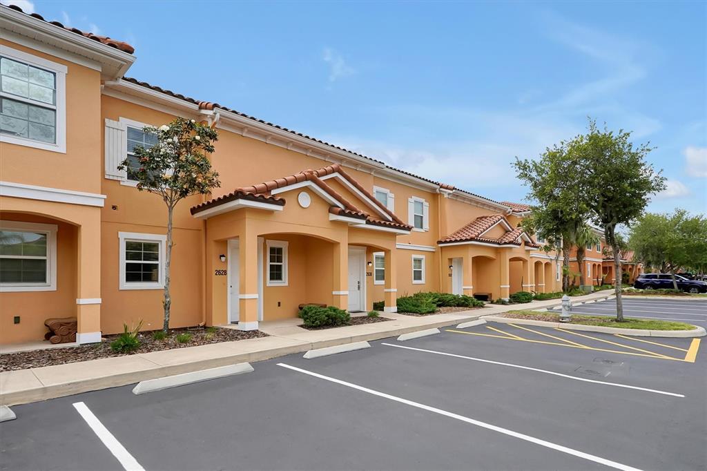 A row of two-story tan stucco townhomes with tiled roofs and adjacent parking spaces — 2628 ROADSTER LANE, KISSIMMEE, FL