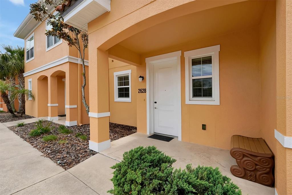 The exterior of a peach-colored townhouse features a covered entryway with a white front door — 2628 ROADSTER LANE, KISSIMMEE, FL