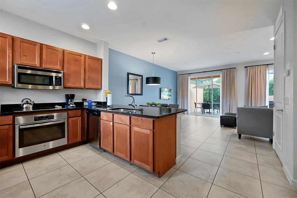 A kitchen with wood cabinets and a granite island opens to a dining and living area — 2628 ROADSTER LANE, KISSIMMEE, FL