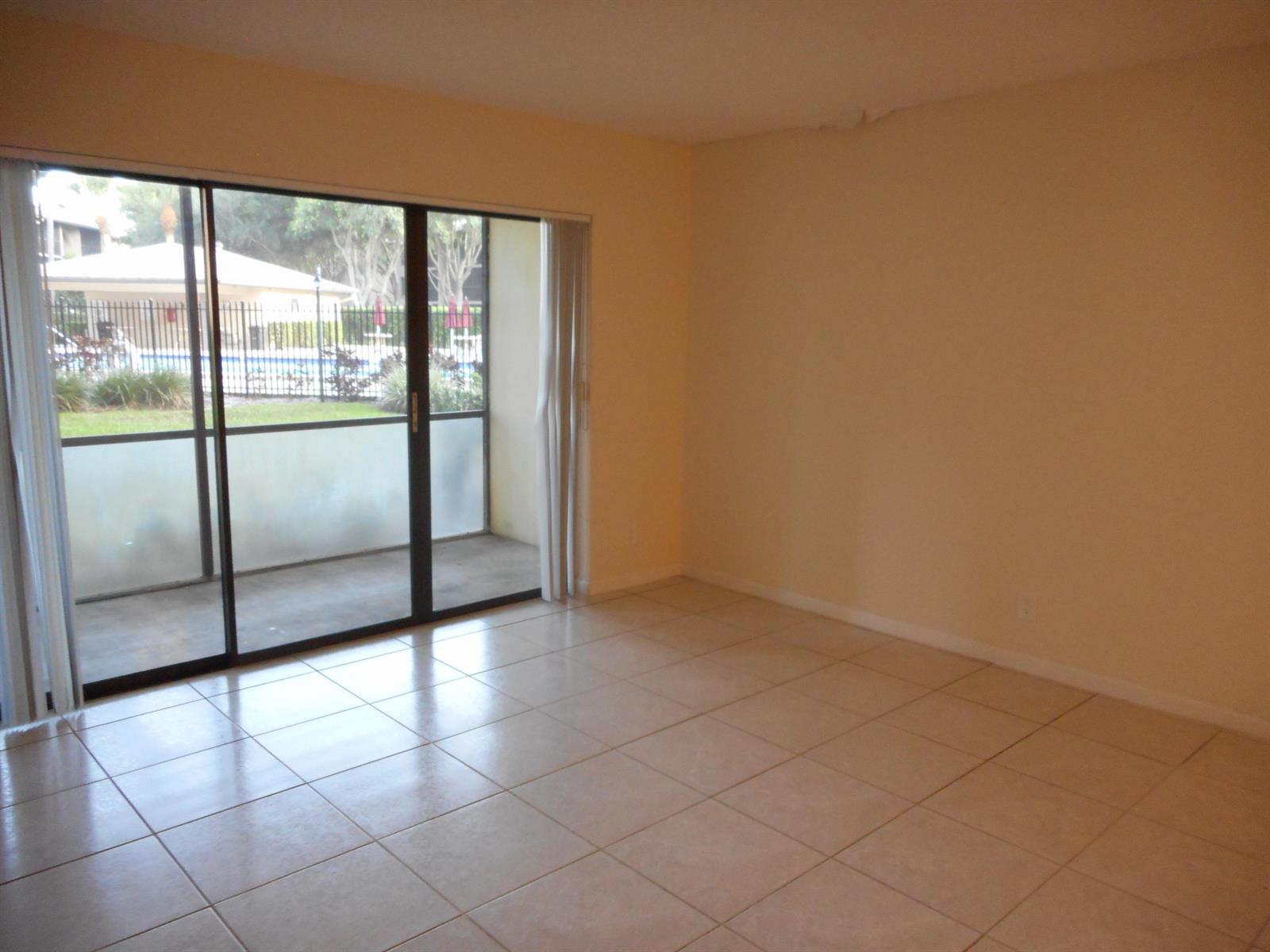 An empty room with beige tile flooring and a sliding glass door leading to a patio — 202 Foxtail Drive # F1, FL 33415, FL