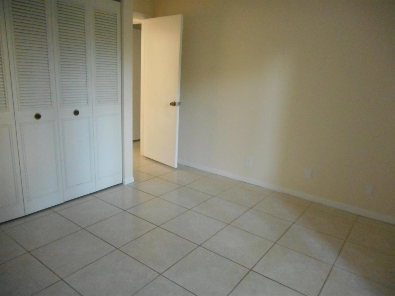 An empty room with light-colored tile flooring, beige walls, and white louvered closet doors — 202 Foxtail Drive # F1, FL 33415, FL