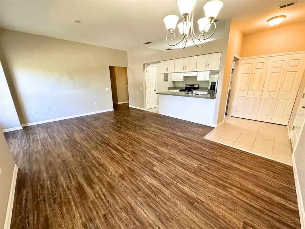 An open-concept living area features wood-look flooring, a kitchen with white cabinets, and a chandelier — 1005 EAGLE POND DRIVE UNIT 1005, WINTER HAVEN, FL