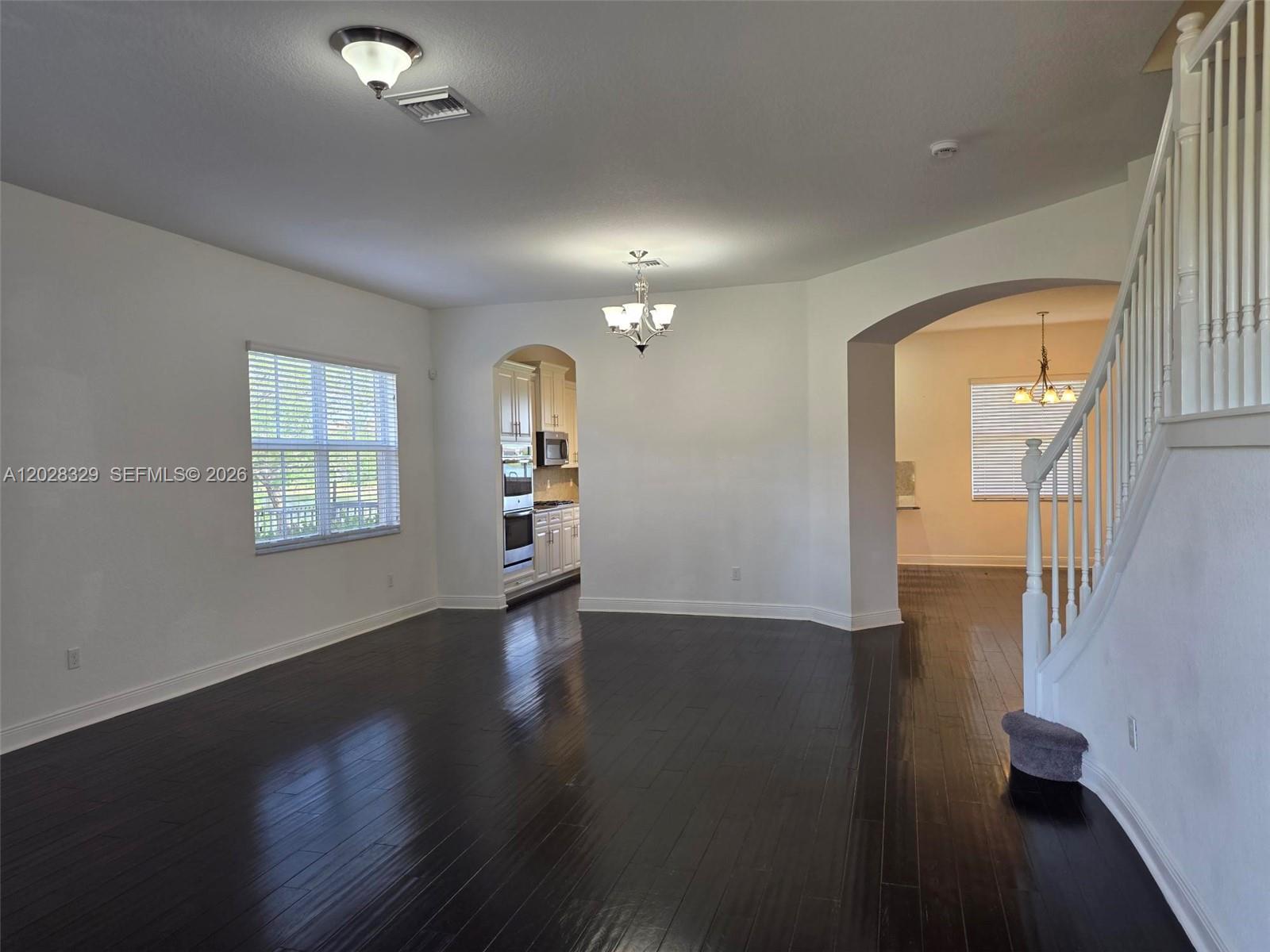 A living room with dark hardwood floors, white walls, and an adjacent kitchen area — 8671 Lakeside Bnd # 1, Parkland FL 33076, PARKLAND, FL