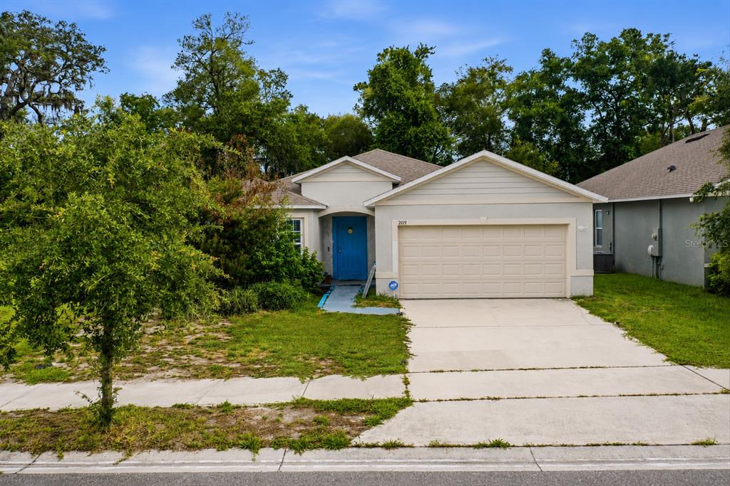 A single-story house with a beige garage, blue front door, and a concrete driveway — 209 MEGHAN CIR, DELAND, FL