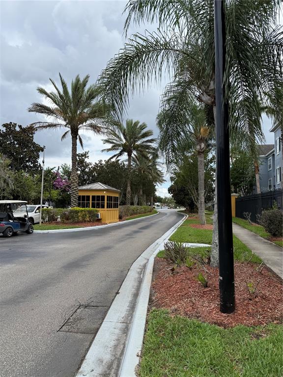 A paved road leads toward a yellow guardhouse surrounded by palm trees and landscaping — 3725 CONROY ROAD UNIT 2127, ORLANDO, FL
