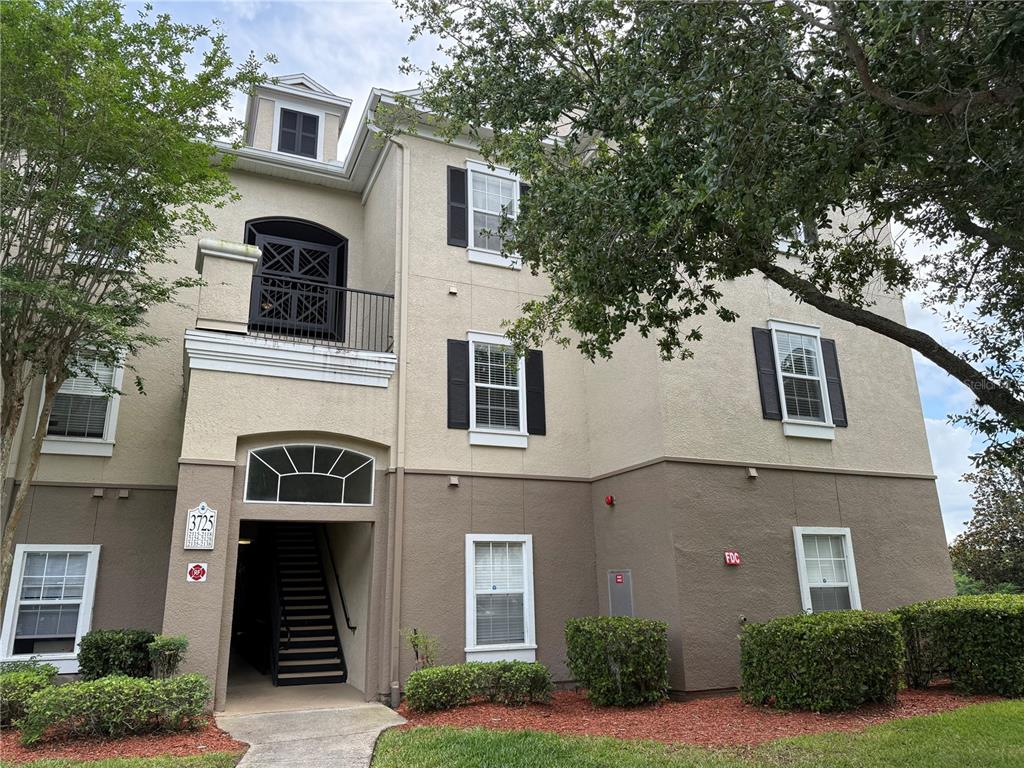 A three-story apartment building exterior features tan stucco walls, black shutters, and a stairwell entrance — 3725 CONROY ROAD UNIT 2127, ORLANDO, FL