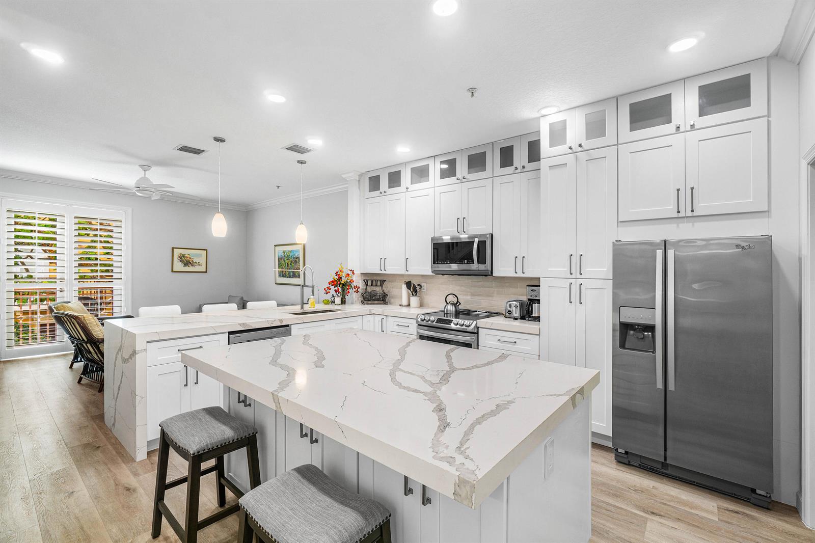 A modern kitchen features white cabinetry, a large marble-topped island, and stainless steel appliances — 65 SE 5th Avenue, Delray Beach FL 33483, DELRAY BEACH, FL