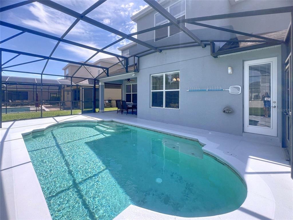 A swimming pool sits on a patio enclosed by a screened-in lanai behind a house — 1476 LEXINGTON AVE, DAVENPORT, FL