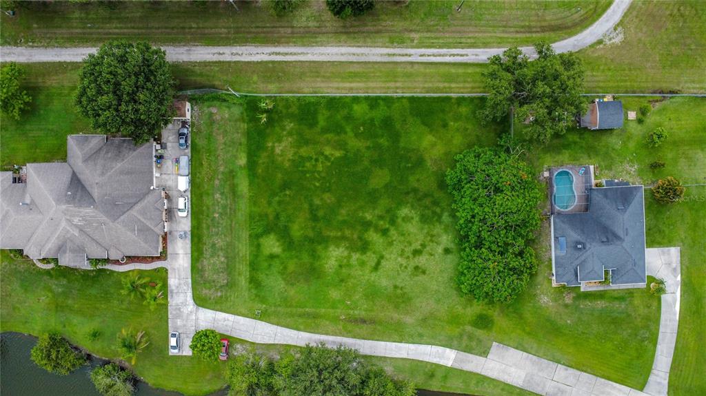 An aerial view shows a vacant grassy lot situated between two houses with driveways — 2959 MONICA TERRACE, KISSIMMEE, FL