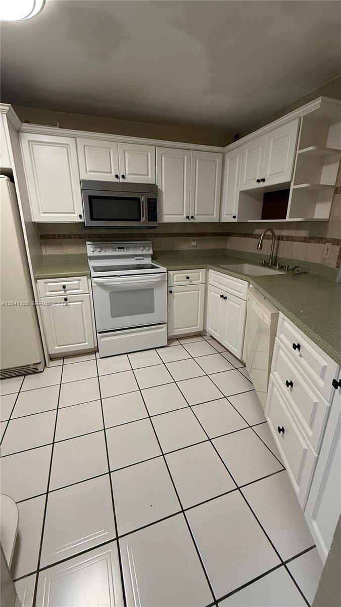 A kitchen features white cabinetry, a stainless steel microwave, a white stove, and tiled floors — 1770 NE 191st St # 1, Miami FL 33179, MIAMI, FL