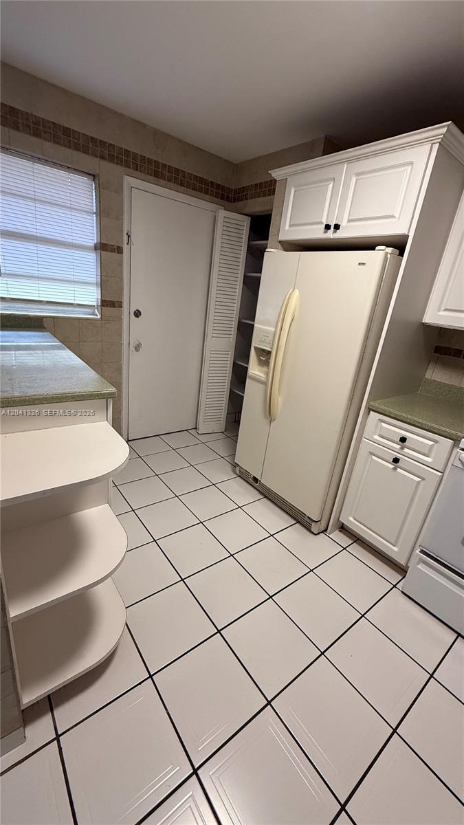 A kitchen features white cabinets, a side-by-side refrigerator, tiled flooring, and a pantry closet — 1770 NE 191st St # 1, Miami FL 33179, MIAMI, FL