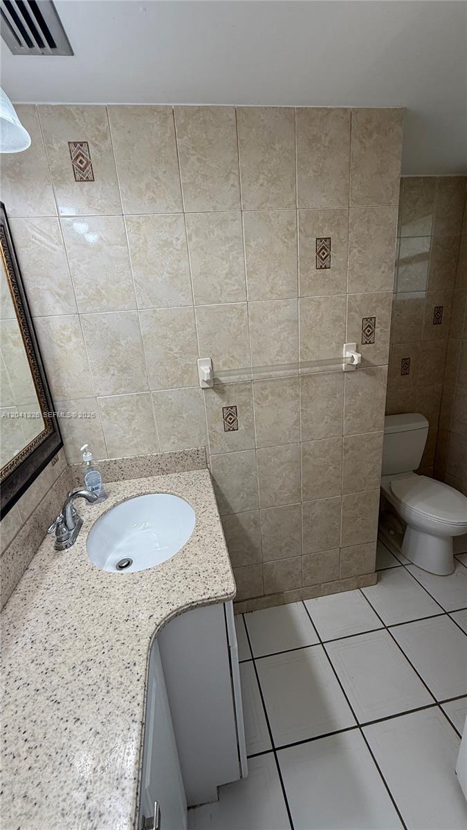 A bathroom features a vanity with a speckled countertop, a toilet, and beige tiled walls — 1770 NE 191st St # 1, Miami FL 33179, MIAMI, FL