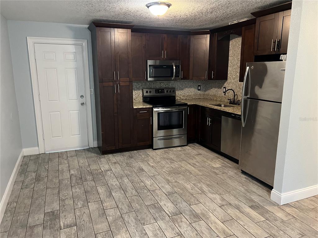 A kitchen features dark wood cabinets, stainless steel appliances, granite countertops, and wood-look tile flooring — 920 MAYDELL DRIVE UNIT B, TAMPA, FL