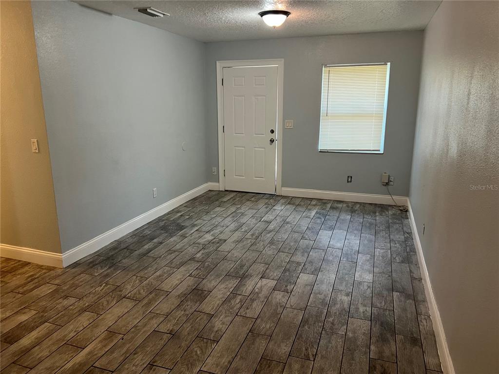 An empty room features light blue walls, wood-look tile flooring, a white door, and a window — 920 MAYDELL DRIVE UNIT B, TAMPA, FL