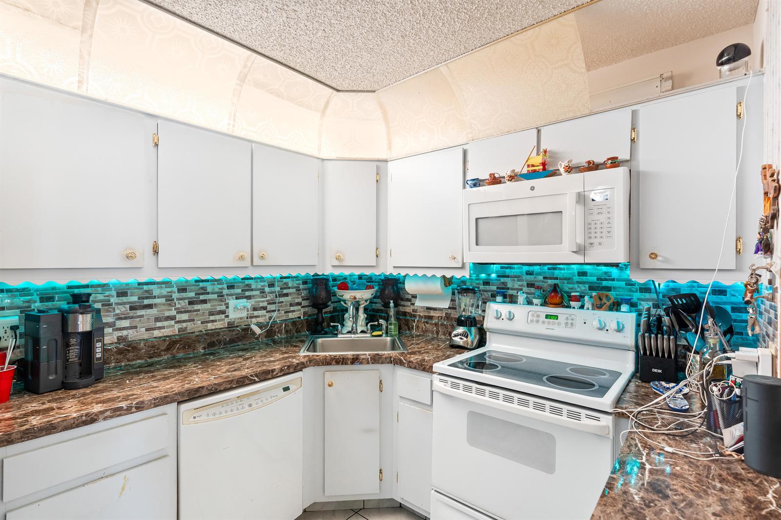 A kitchen with white cabinets, marble-patterned countertops, a tiled backsplash, and under-cabinet blue lighting — 4996 Sable Pine Circle # A1, West Palm Beach FL 33417, WEST PALM BEACH, FL