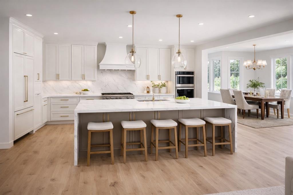 A modern kitchen features white cabinetry, a marble-topped island with stools, and light wood flooring — 1106 SARAH MATHEWS DRIVE, OAKLAND, FL