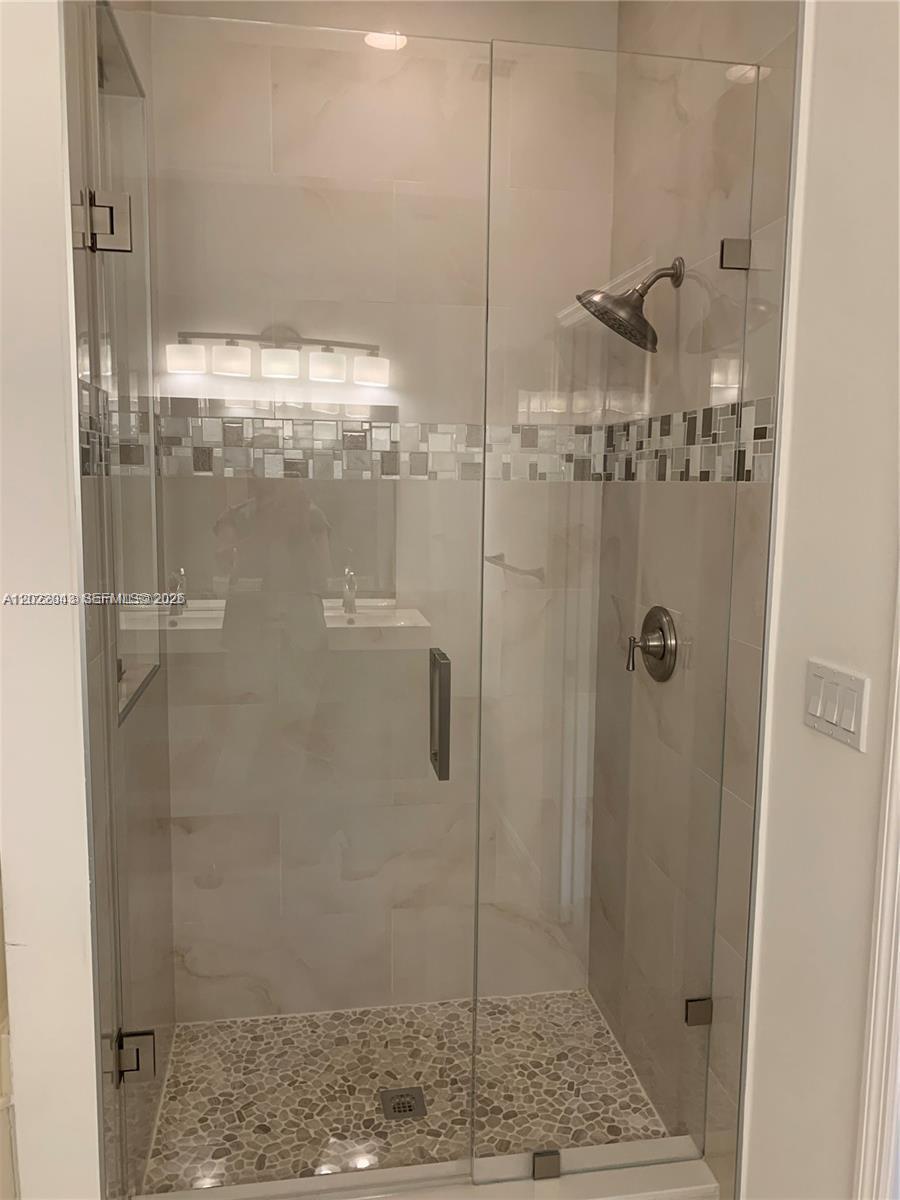 A glass-enclosed shower features light-colored wall tiles, a pebble floor, and a brushed nickel showerhead — 649 NE 33rd Ter # 649, Homestead FL 33033, HOMESTEAD, FL
