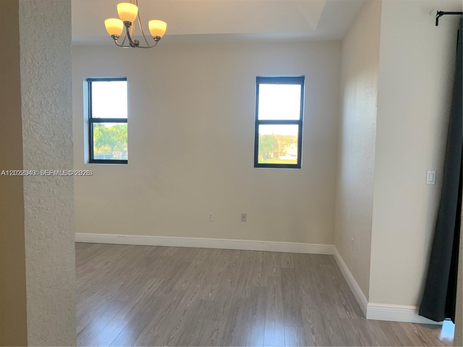 An empty room features light wood-look flooring, two windows, and a hanging light fixture — 649 NE 33rd Ter # 649, Homestead FL 33033, HOMESTEAD, FL