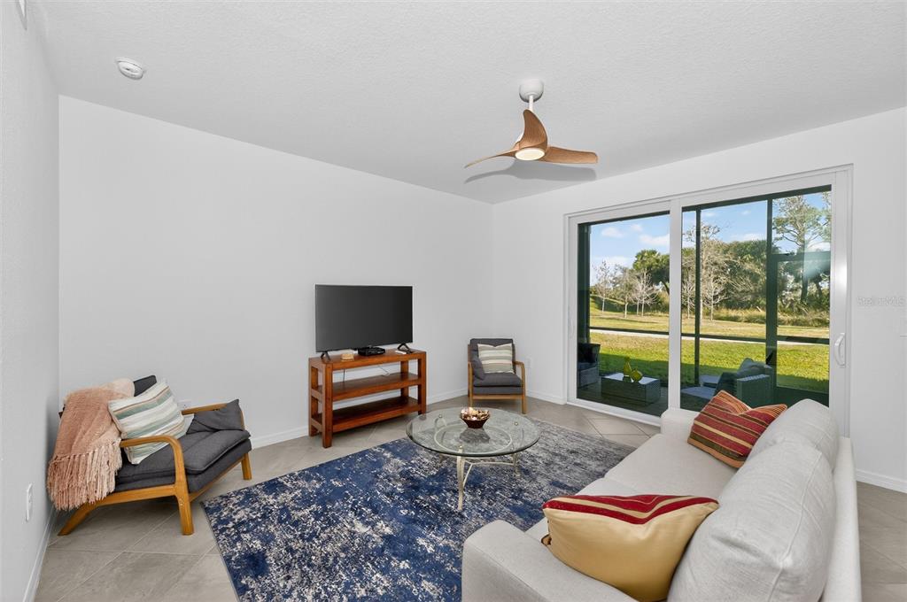 A living room features a sofa, two armchairs, a television, and a sliding glass door — 12520 GALAPAGOS COURT UNIT 105, VENICE, FL