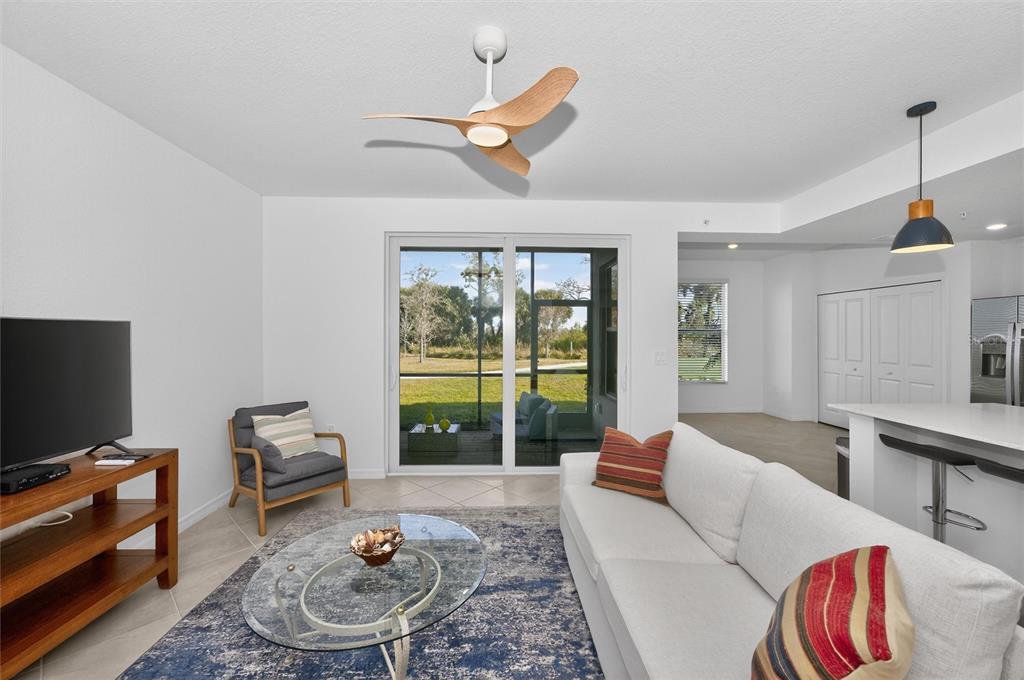 A living room features a white sofa, glass coffee table, wood media console, and ceiling fan — 12520 GALAPAGOS COURT UNIT 105, VENICE, FL