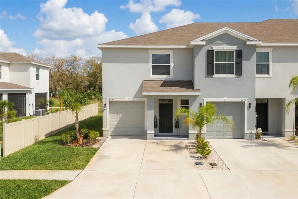A two-story duplex with gray stucco siding, two garages, and a concrete driveway — 1287 COLT CREEK PLACE, WESLEY CHAPEL, FL