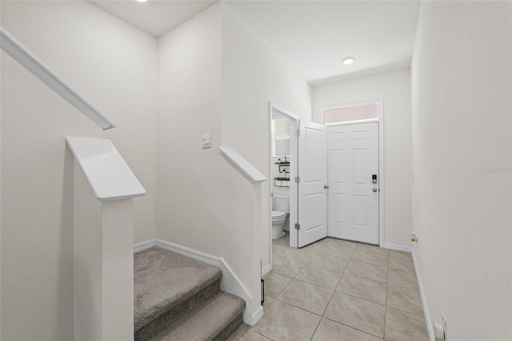 An entryway features tile flooring, a carpeted staircase, and a door leading to a bathroom — 1287 COLT CREEK PLACE, WESLEY CHAPEL, FL