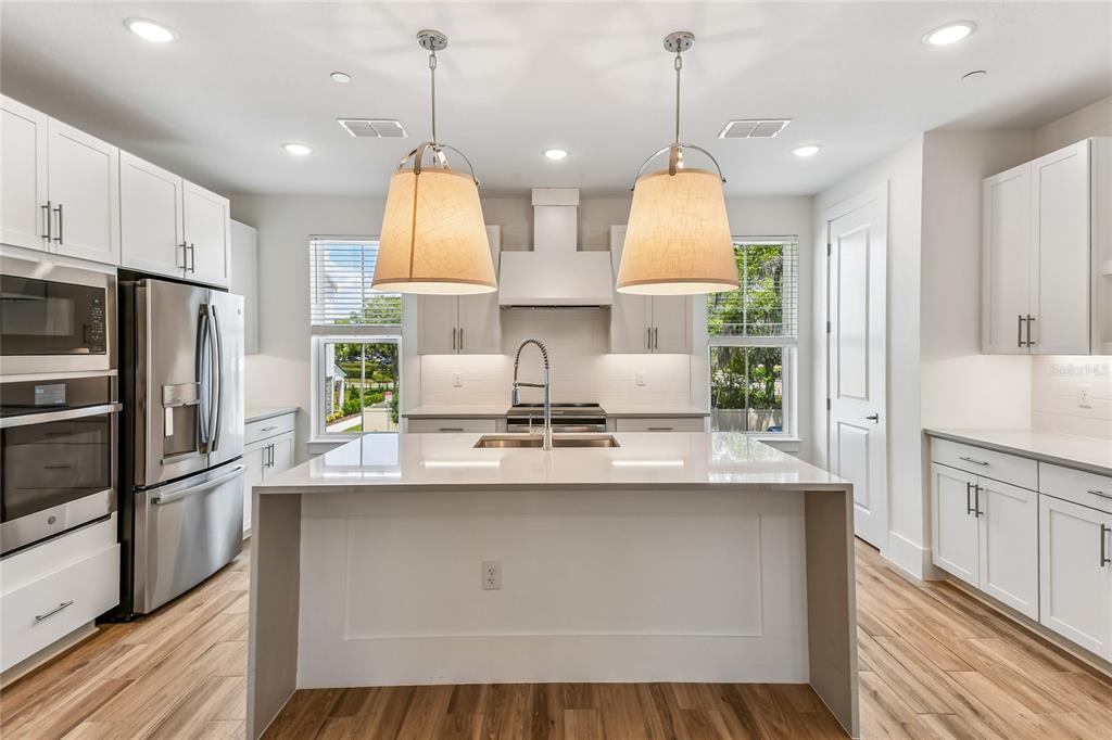 A modern kitchen features a white island, stainless steel appliances, and light wood flooring — 202 PASQUALA, OVIEDO, FL